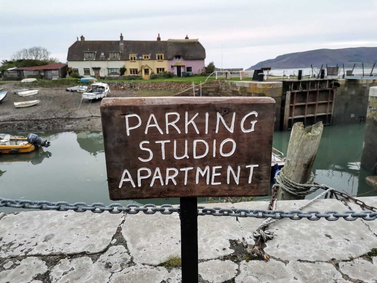 Schild für ein 'PARKING STUDIO APARTMENT' mit Blick auf Boote und ein Gebäude im Hintergrund.
