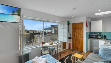 Une chambre moderne dotée d’une grande fenêtre donnant sur la côte, d’une petite kitchenette et d’un coin salon avec une table et des chaises.
