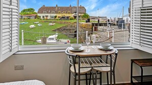 Quarto com uma grande janela com vista para um porto, uma mesa de jantar com cadeiras e uma cama.