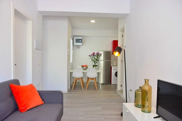 A living room with a grey sofa, a red pillow, a TV, and two glass bottles on a white table.