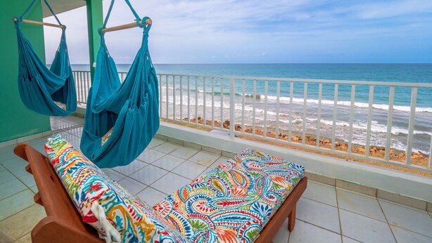 A balcony with a view of the ocean, a hammock, and a colorful sofa. - Jewel in the sky, joy on the beach: beachfront penthouse, views of El Yunque (Luquillo)