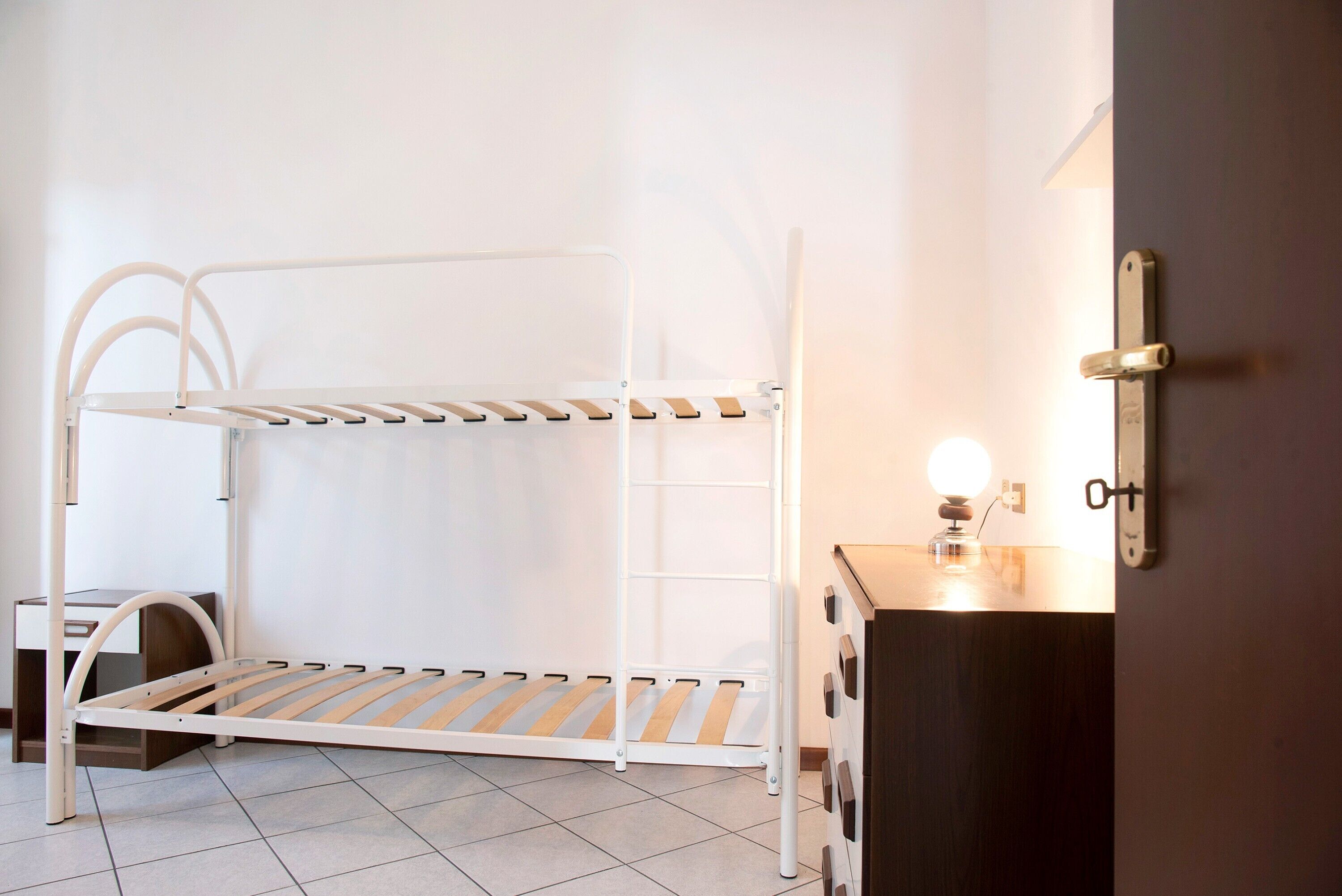A bunk bed with a desk and dresser, a wall-mounted light, and a door.