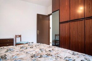 Une chambre à coucher avec un lit, une armoire en bois, une chaise et une porte.