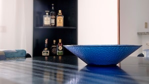 Eine blaue, strukturierte Schale auf einer dunklen Oberfläche, ein schwarzes Regal mit Flaschen im Hintergrund und ein blaues Sofa.