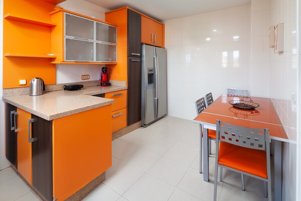 Una cocina moderna con armarios color naranja, un refrigerador de acero inoxidable y una mesa de comedor con sillas.