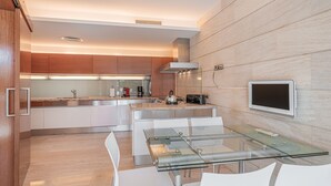 A modern kitchen with a glass dining table, white chairs, and a built-in TV. - Villa Agusmar with Sea View, Pool & Wi-Fi (llucmajor)