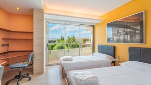 A hotel room with two beds, a desk, a chair, a balcony with a view, and a cityscape painting on the wall. - Villa Agusmar with Sea View, Pool & Wi-Fi (llucmajor)