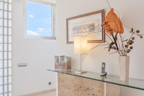 Een receptiebalie met een glazen bureau, een lijst met foto, een lamp en een vaas met gedroogde planten.