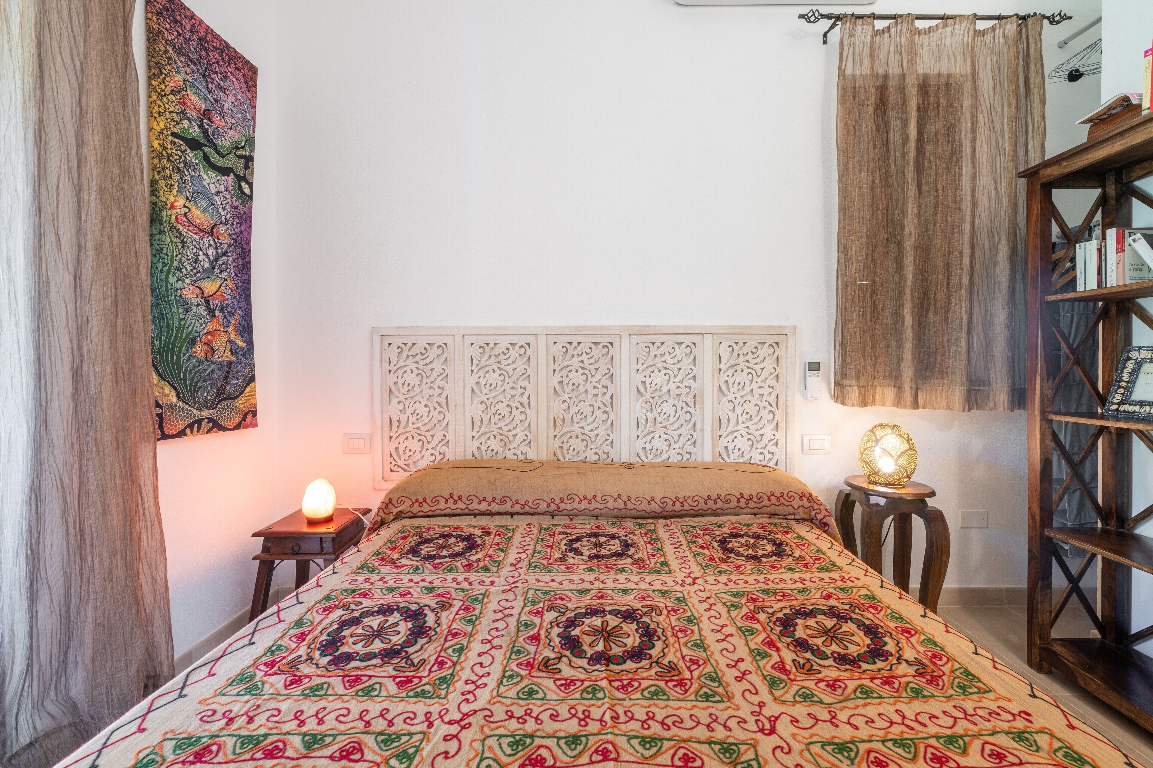 Un lit avec une couvre-lit à motifs, une lampe de chevet, une décoration murale et une bibliothèque en bois.