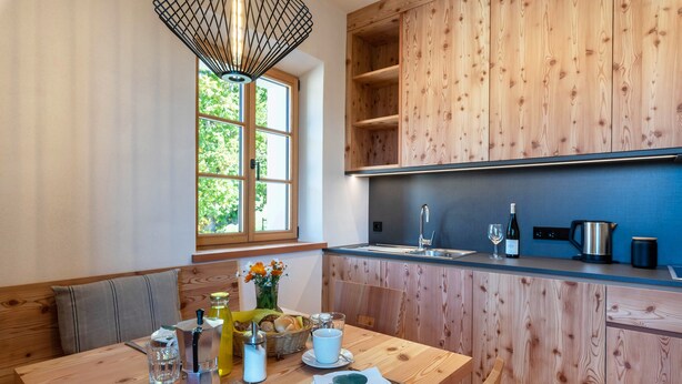A modern kitchen with wooden cabinetry, a dining table set with glassware, and a window with a view of greenery. - Holiday Apartment Hof im Thal Apt Linde with Mountain View, Balcony & Wi-Fi (Aldino)