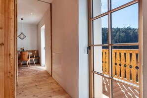 A hallway leading to a dining area with a wooden floor, a hanging light fixture, and a view of a wooden deck outside.