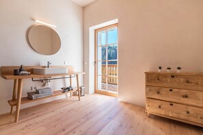 Un bagno con un mobile bagno in legno, uno specchio rotondo, un lavandino e un settimino in legno.