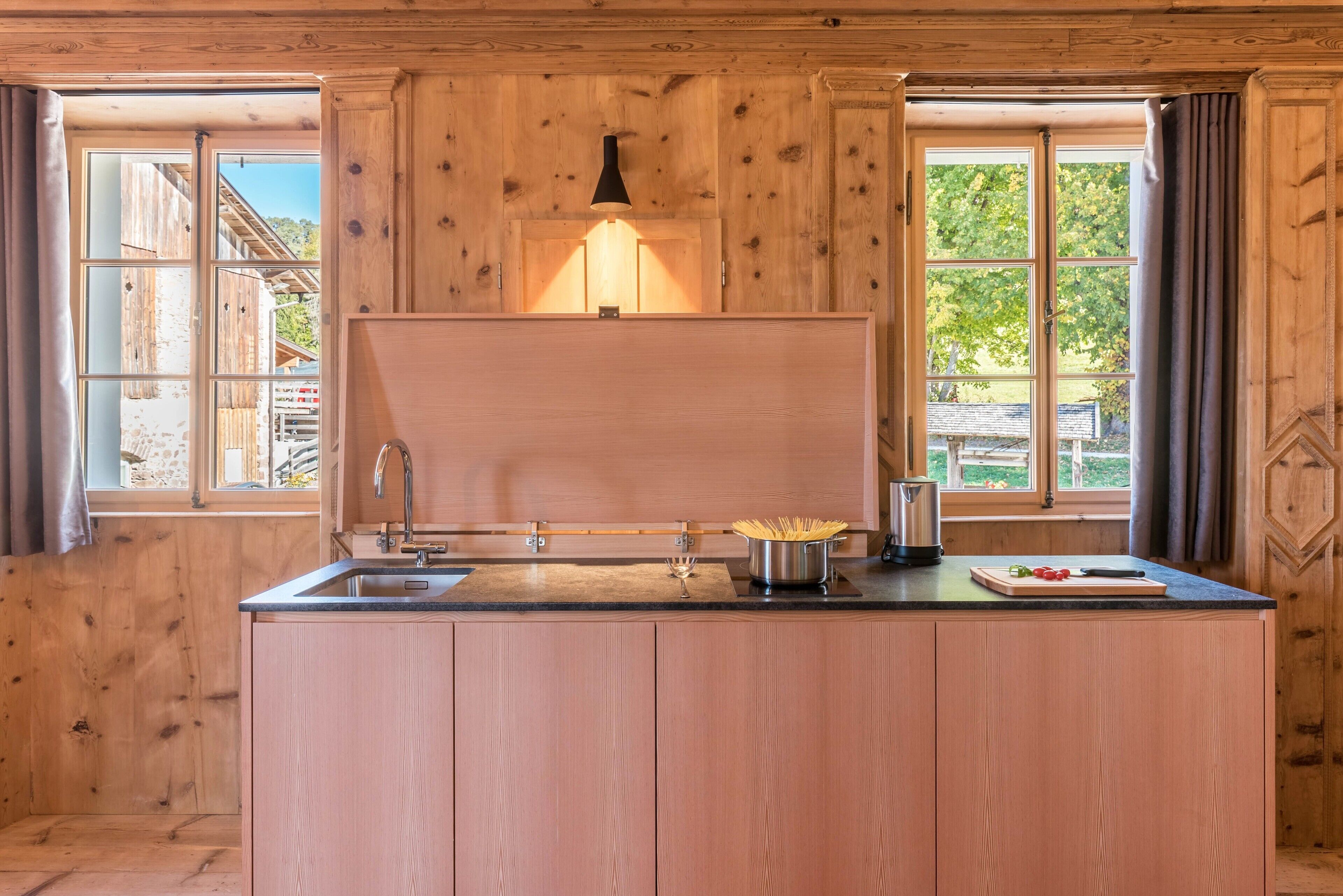 Een houten keuken in chaletstijl met een centraal eiland, een hanglamp en grote ramen.