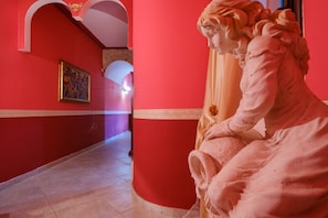 A hallway with red walls, a statue, and a framed artwork.