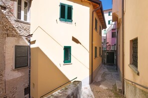 Une ruelle étroite, située entre des bâtiments aux murs de pierre et aux volets fermés.