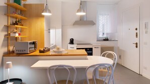 A modern kitchen with a wooden shelf, a white countertop, a built-in oven, and a white dining table with chairs.