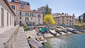A waterfront with boats docked, stone steps leading down to the water, and buildings with balconies and shutters.