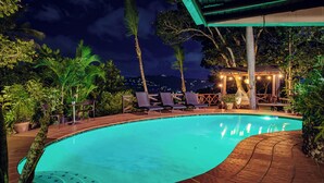 A swimming pool with lounge chairs and a covered seating area, surrounded by tropical vegetation. - Green Nest at the Hills (Guaynabo)