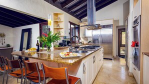 A modern kitchen with granite countertops, stainless steel appliances, and a central island with bar stools. - Green Nest at the Hills (Guaynabo)
