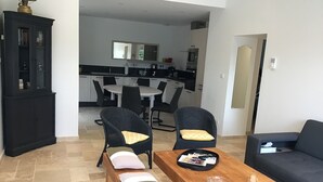 Una sala de estar moderna con una mesa de centro de madera, dos sillones de mimbre con cojines, un sofá oscuro y un mueble negro.