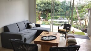 Una sala moderna con un sofá seccional gris, dos sillas de mimbre negro, una mesa de centro de madera y una mesa de vidrio con un control remoto.