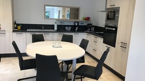 Una cocina moderna con una mesa de comedor redonda, sillas negras y armarios de color claro.