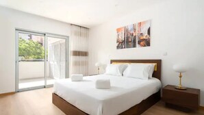 A modern hotel room with a large bed, a nightstand, and a view through a sliding glass door.