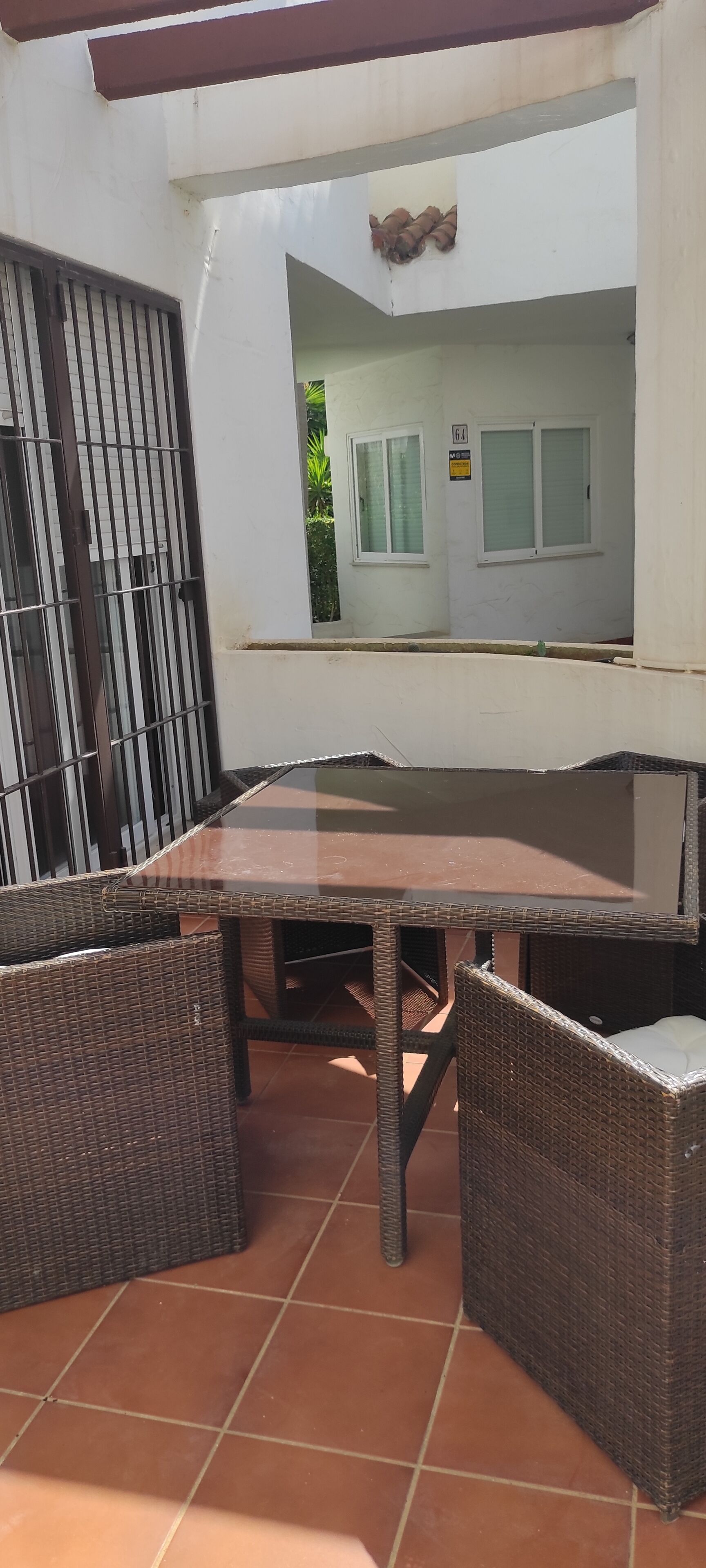 Un patio con mesa y sillas de mimbre, suelo de baldosas y vistas a un edificio con ventanas y puerta.