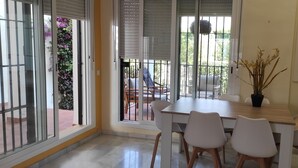 Un coin repas comprenant une table et quatre chaises, une plante en pot, et une vue sur le balcon extérieur, où se trouvent une chaise et une table.