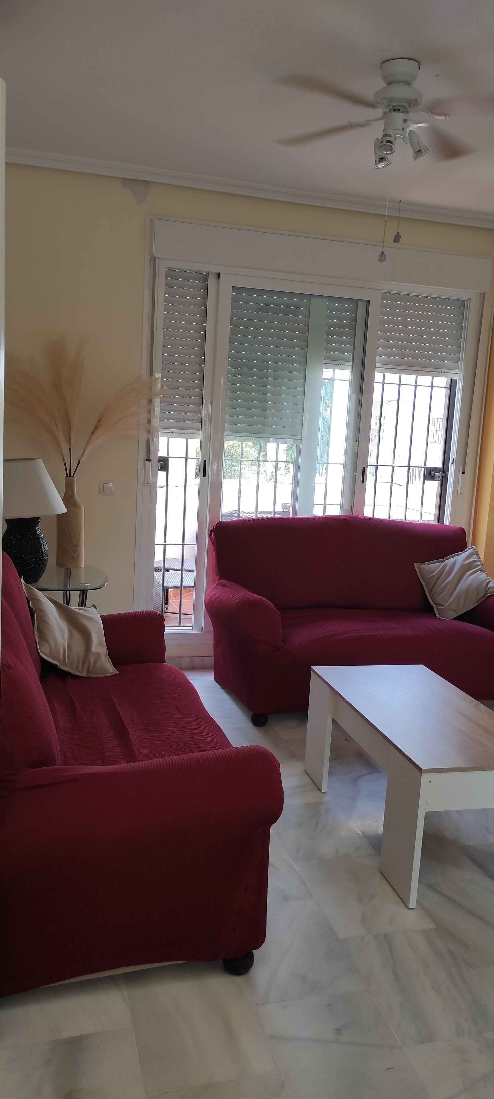 A living room with two red sofas, a white coffee table, and a ceiling fan.