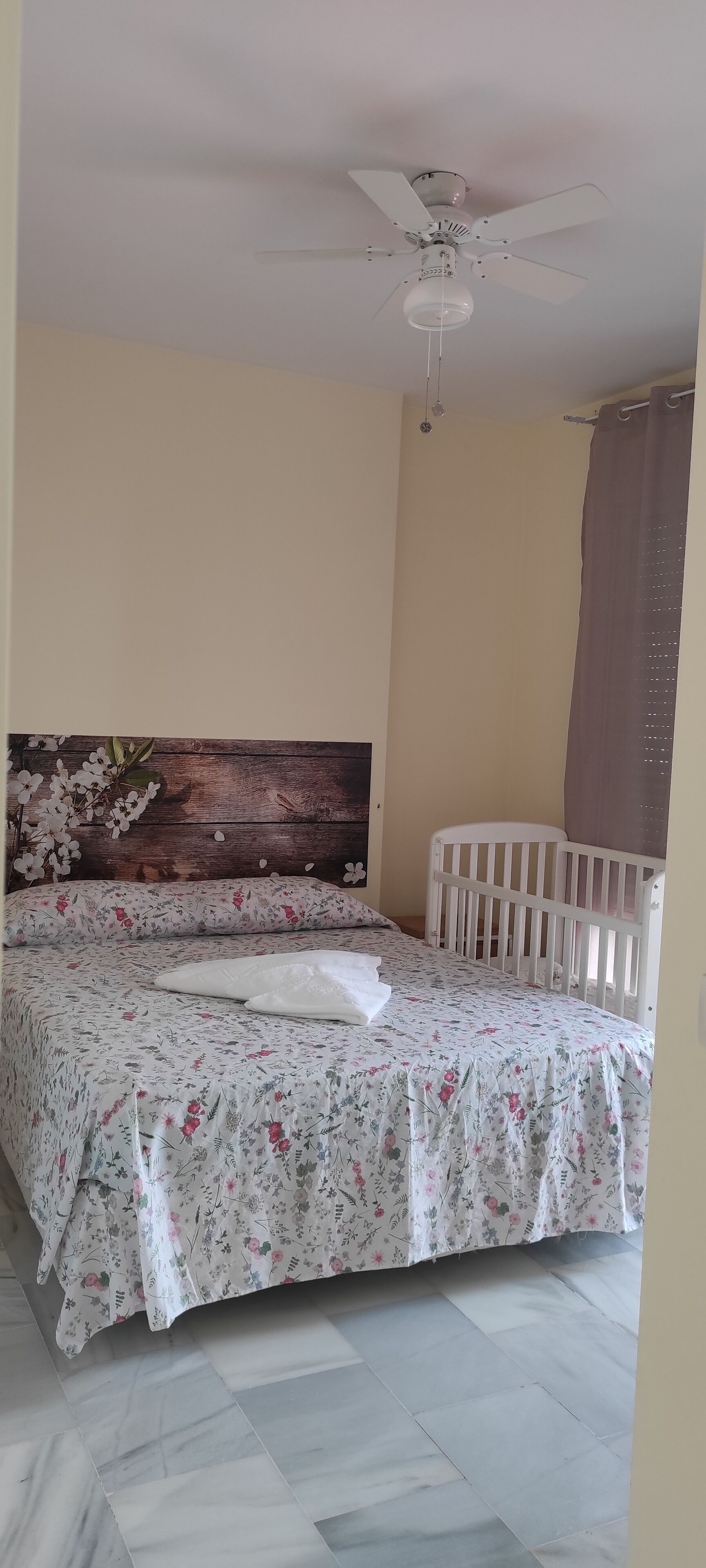 Een slaapkamer met een bed, een plafondventilator, een wieg en een houten hoofdbord.