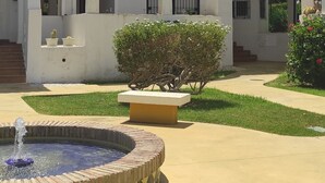 Une cour avec une fontaine, un petit arbuste et un bâtiment doté d’un toit en tuiles et d’une antenne parabolique.