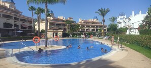Ein Schwimmbeckenbereich mit mehreren Pools, Palmen und einem Gebäude mit Kuppel im Hintergrund.