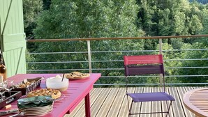 Una terraza de madera con una mesa lista para comer, una silla y vistas a una cadena montañosa boscosa.