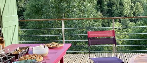 A wooden deck with a table set for dining, a chair, and a view of a forested mountain range.