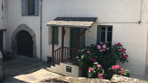 Un edificio blanco con un pequeño porche, un arco de piedra y un jardín de flores rosadas.