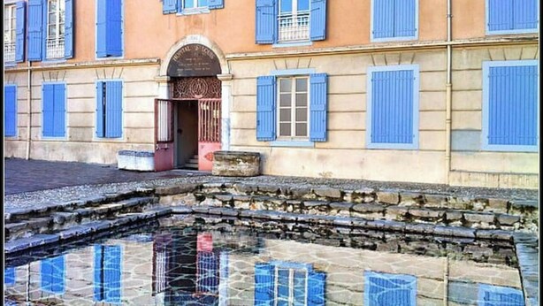 Un edificio con contraventanas azules y una fuente de piedra en su fachada.