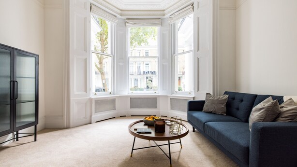 Een woonkamer met een donkerblauwe bank, een ronde salontafel met een boek en een schaal, en een zwarte kast.