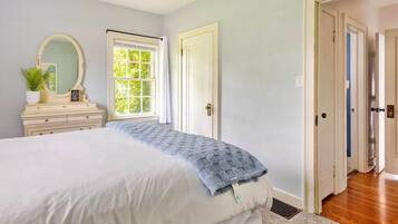 Une chambre à coucher avec un lit, une commode, un miroir et une fenêtre.