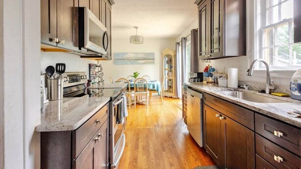 A kitchen with wooden cabinets, stainless steel appliances, and a wooden dining table with chairs. - Large House w/King Bed, Parking, Deck, Restaurants (Indianapolis)