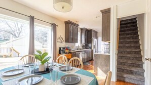 A dining area with a table set for four, a kitchen in the background, and a staircase leading to another level. - Large House w/King Bed, Parking, Deck, Restaurants (Indianapolis)