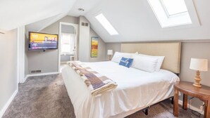 A bedroom with a large bed, a TV mounted on the wall, a skylight, and a small bedside table. - Large House w/King Bed, Parking, Deck, Restaurants (Indianapolis)