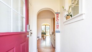 A hallway with a red door, a welcome sign, and a plant on the windowsill. - Large House w/King Bed, Parking, Deck, Restaurants (Indianapolis)