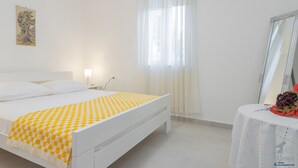 Un dormitori amb un llit, una taula de nit amb mirall, una finestra amb cortines i una obra d'art penjada a la paret.