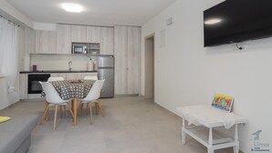 Una cuina moderna amb zona de menjador, un televisor de pantalla plana penjat a la paret i una taula petita amb un llibre.