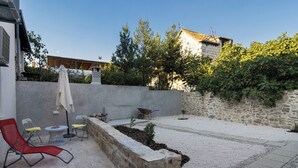 Un pati exterior amb mur de pedra, una cadira relaxant vermella, una taula petita i una carreta.