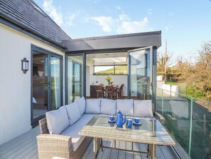 A modern outdoor seating area with a glass table and wicker furniture, overlooking a dining area and a scenic landscape. - 3 bedroom accommodation in Bryn Pydew, near Llandudno (Bryn Pydew, near Llandudno)