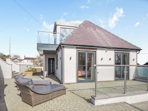 Une maison moderne dotée d’un balcon, d’une porte vitrée et d’un petit espace extérieur aménagé pour s’asseoir.