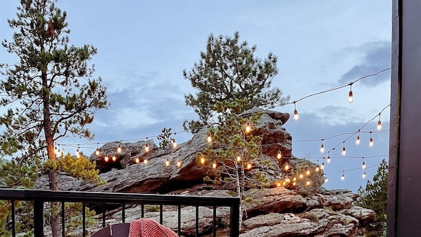 An outdoor seating area with a fire feature, a chair with a blanket, and string lights.