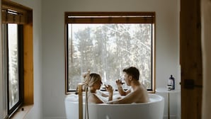 A modern bathroom with a freestanding bathtub, large windows, and a view of trees.